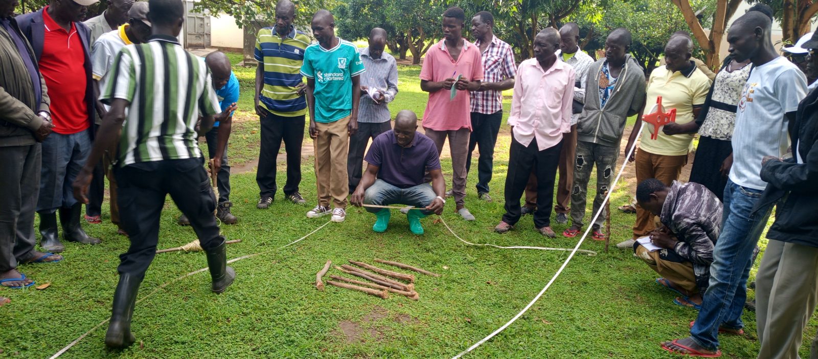 Cocoa farmers and agriculture students participate in a practical field lesson on cocoa plantation layout, spacing and digging planting holes at Jabara Agricultural Vocational Institute in Koboko.