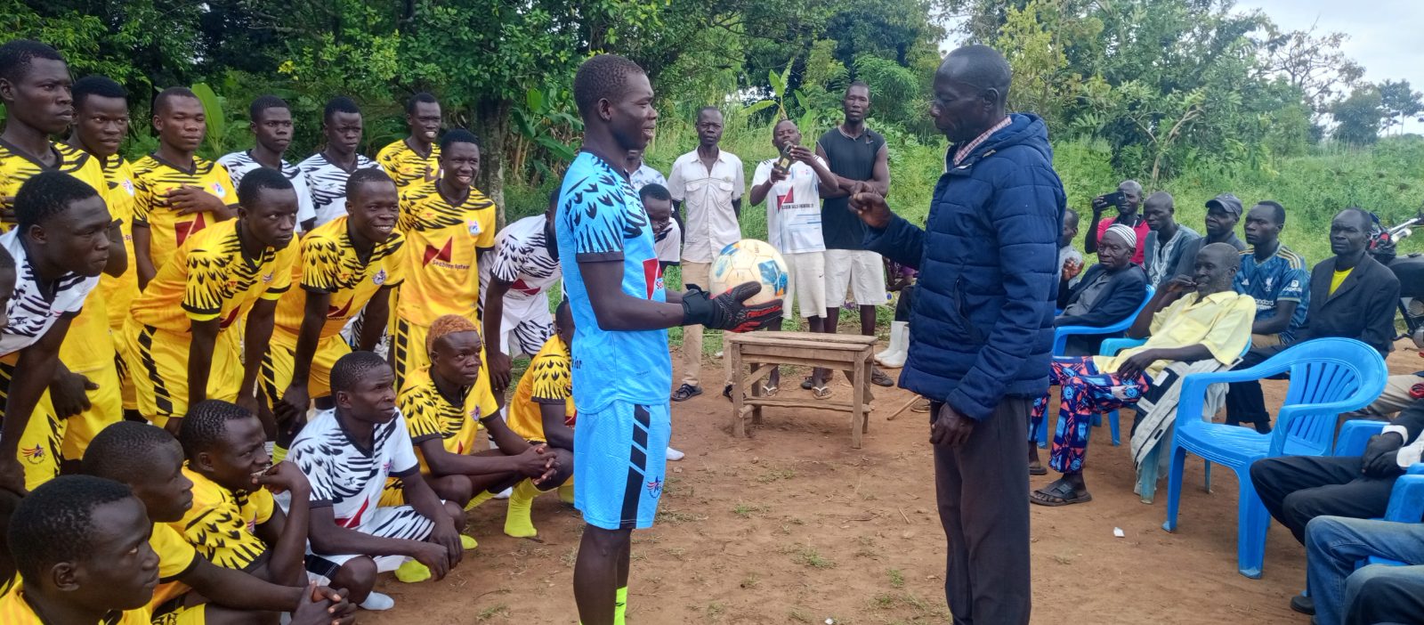 Alt text: Seaborn Star FC captain and goalkeeper receives a football from Pajama elder Avua Lino during blessing prayers for the team ahead of the 2026/27 season in Ajumbiri Village, Yumbe District.