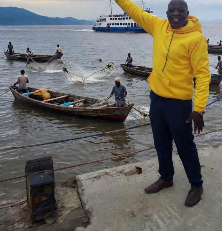 A weathered concrete jetty stretching into the brown waters of Lake Albert, Uganda, with green hills behind and the hazy Congolese shoreline beyond the horizon