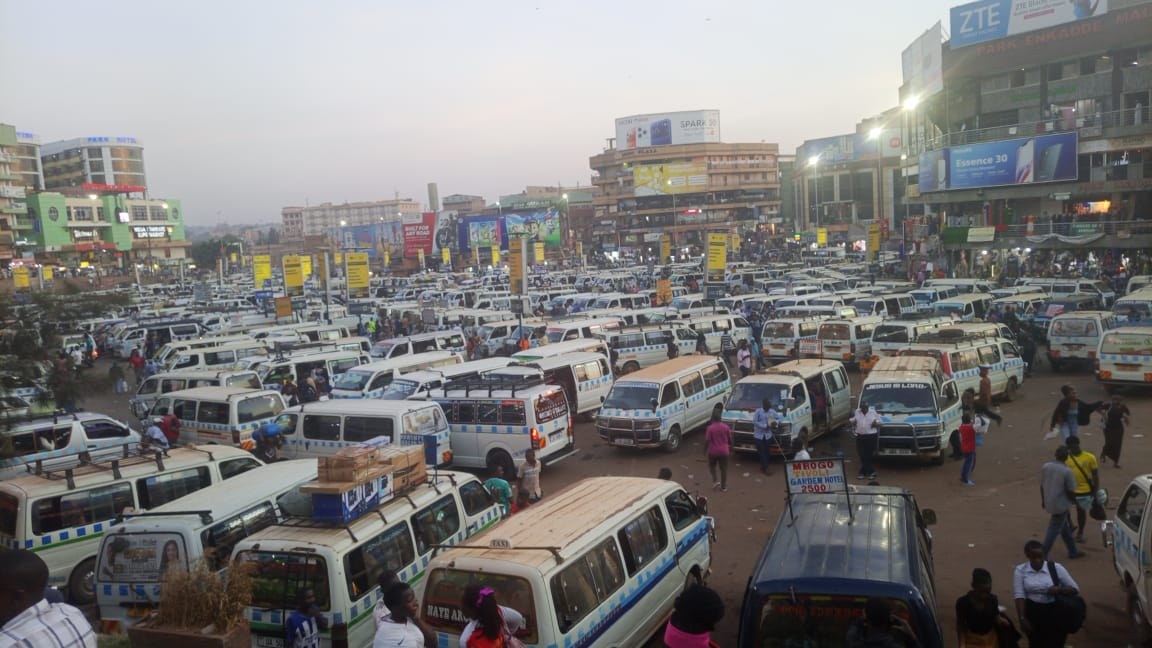 White-and-blue minibus taxis crowding Kampala's Old Taxi Park as commuters weave between vehicles